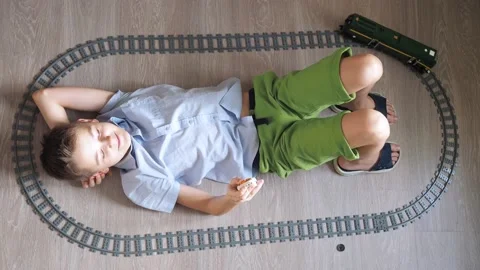 A boy is playing with a train on the controls on the floor in the room. top view Stock Footage 171129674