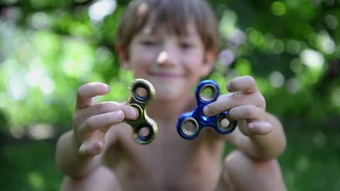 Boy playing with two fidget spinner stress relieving toys outdoor Stock Footage 80194713