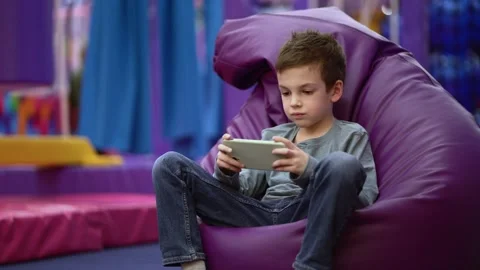 Boy playing a video game on a handheld console while sitting in a large bag 動画素材 337006324