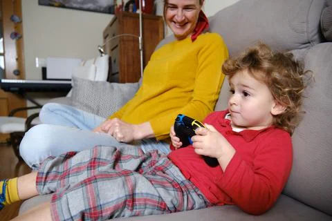 Boy playing video games while his mother watches Stock Photos