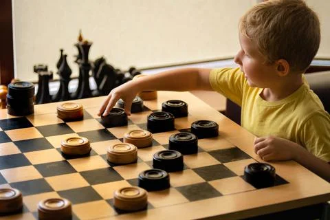 Boy plays checkers and makes a move with his hand. Chess board with checkers. Stock Photos