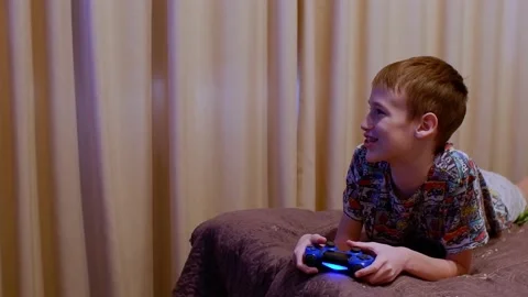 The boy plays the console lying on the bed. Home entertainment. Stock Footage 169601443