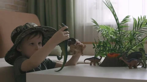 A boy plays with dinosaur figurines on the table. The little explorer in the  Stock Footage 147672898