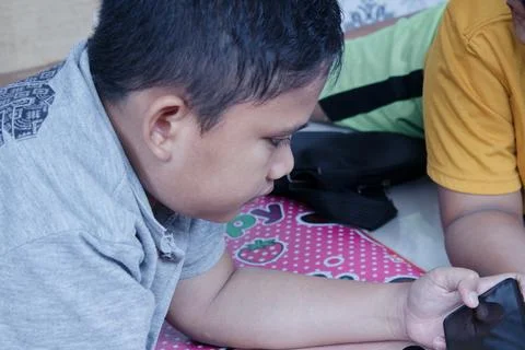 A boy plays with his cellphone while lying down Stockfoto's