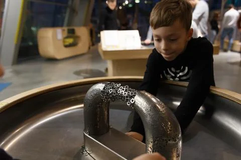 A boy plays with metal objects on a stand with a large magnet Фото