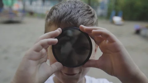 The boy plays with ND lens filter and puts it to the camera. Exposure adjust Stock Footage 95148300