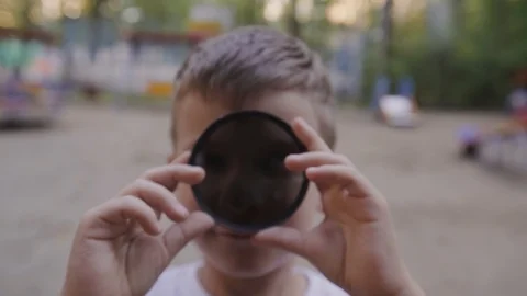 The boy plays with ND lens filter and puts it to the camera. Exposure adjust Stock Footage 95148347