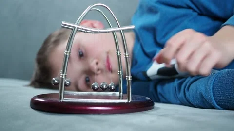 A boy plays with a Newton's pendulum balls lying on divine Stock Footage 146976826