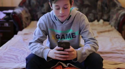 A boy plays in the phone sitting on the sofa Video stock 50965804