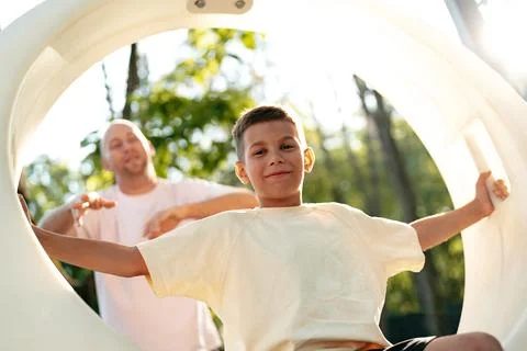 Boy plays on playground slide while adult supervises in sunny park Stock Photos