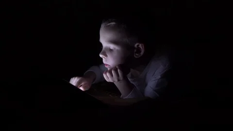 The boy plays on the tablet in complete darkness, lying on the bed. Stock Footage 99146990