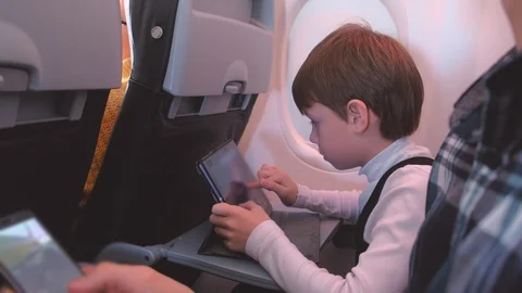 Boy plays on the tablet during the flight in the plane. Dad looks at phone. Video stock 116590449