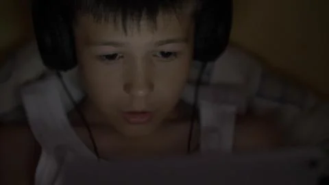 Boy plays on the Tablet lying in the dark in headphones Stock Photos