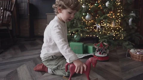 The boy plays with a toy horse near christmas tree Stock Footage