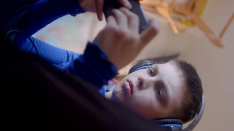 A boy plays video games on his phone, while an adult lounges with a tablet Stock Footage 313432081