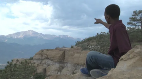 Boy pointing and talking on top of cliff. Video stock 27343083