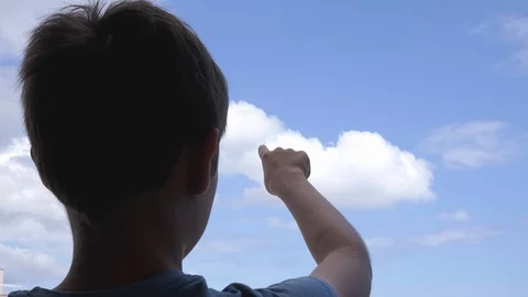 Boy pointing hand to blue sky and draw with finger something in the air Stock Footage 128794927