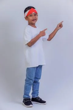 A boy pointing to the side wearing a white shirt, jeans, and a red and whit.. Stock Photos