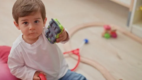 Boy points toy car toward camera with outstretched hand while sitting on fl.. Stock Footage 337433235