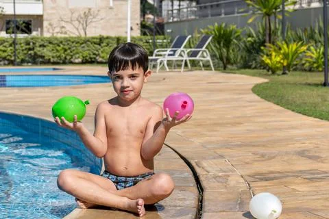 Boy in the pool holding two balloons and looking at the camera. Stock Photos