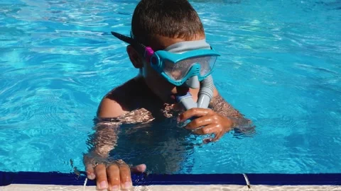 A boy in the pool with a mask and goggles holds on to the edge and dives into Stock Footage 259703790