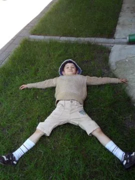 Boy posing lying on the grass, hands to the sides Stock Photos