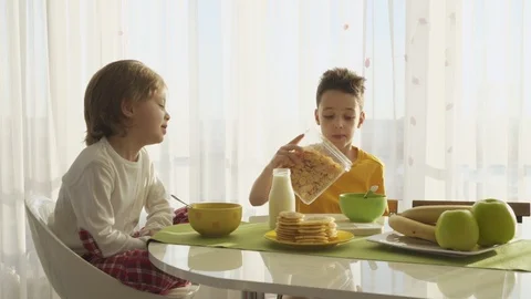 Boy pouring milk in plate with corn flakes, two brothers having breakfast Stockbeeldmateriaal 105090334