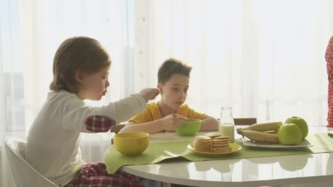 Boy pouring milk in plate with corn flakes, two brothers having breakfast Video stock 105090337
