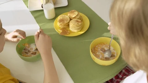 Boy pouring milk in plate with corn flakes, two brothers having breakfast Vidéo 105090365