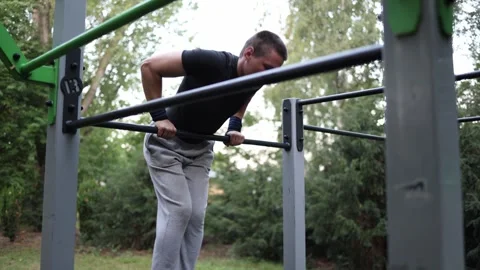 Boy practices calisthenics on horizontal bar outdoors wearing sports clothes foc Stock Footage 316701178