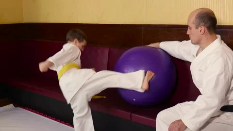 A boy practices a circular kick on a ball held by a coach Stock Footage 268707949