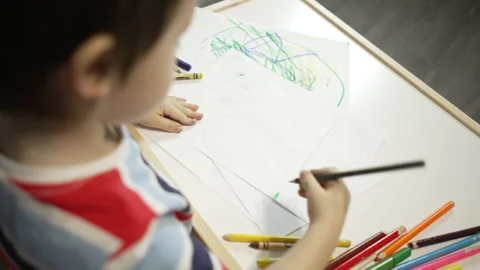 Boy practices drawing with colored pencils at a small table at home 스톡 동영상 152098060
