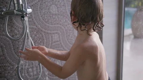 Boy practices hand washing in shower, learning hygiene skills in a bright and Stock Footage 296715339