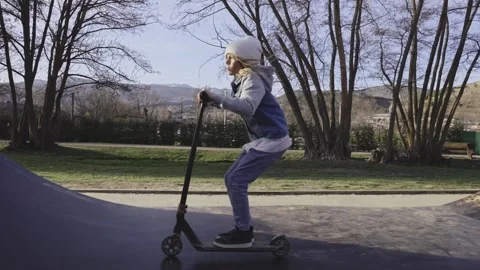 Boy practices riding up down in skate park performing ramp jumps scooter Stock Footage 249905457