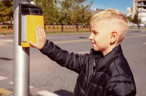 Boy pressing pedestrian crossing button at traffic light on sunny city street Stock Photos