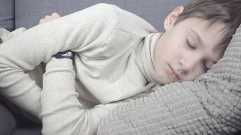 Boy pretending to be sleeping on couch at home. Young boy open eye and looking Stock Footage 148079823