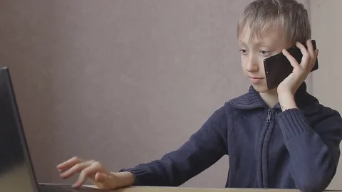 Boy prints on a laptop and talking on the phone Stockbeeldmateriaal 77249332