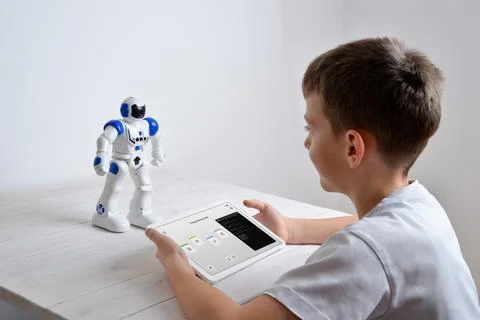 Boy is programming the work of a robot on a desk with a tablet in his hand Foto stock