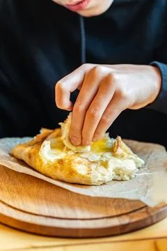Boy pulling cheesy bread from khachapuri on wooden table surface Stock Photos