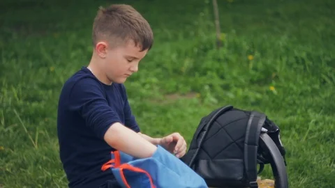 Boy pulling out of the backpack phone on the background of greenery in the park  Video stock 108595082