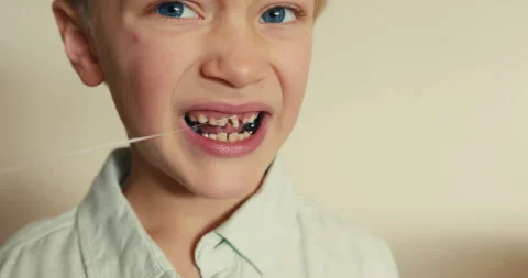 Boy pulling out his loose baby tooth with a string Stock-Footage 346982919