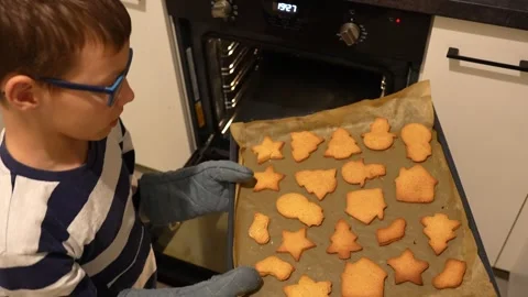 Boy pulls tray of fresh Christmas cookies out of the oven. Stock Footage 297905924