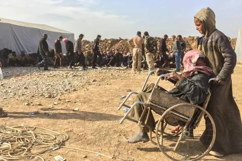 A boy pushes an old man in a broken wheelchair at a screening point Stock Photos