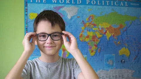 The boy puts on and adjusts his glasses standing against the background of the Stock Footage 167227876