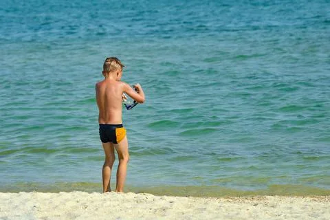 The boy puts on diving goggles on the seashore. 스톡 사진