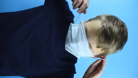 A boy puts on a face mask on a blue background, vertical video Stock-Footage 141393213