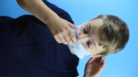 A boy puts on a face mask on a blue background, vertical video Stock Footage 141433834