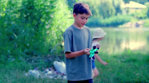 A boy puts on gloves to start cleaning up on the riverbank. Stockbeeldmateriaal 340465164