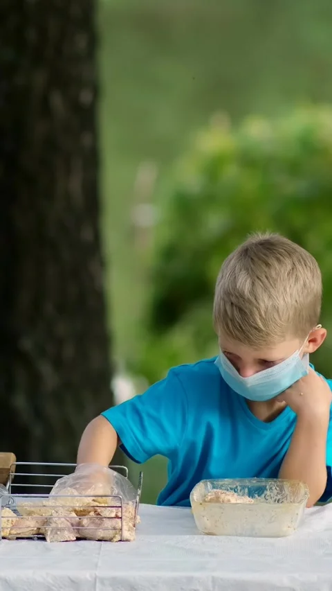 A boy puts marinated meat on the grill grate. Children wearing medical mask.. Stock Footage 305846817