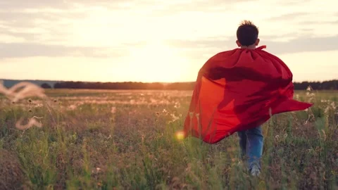 Boy races along field at sunset with raincoat flapping in wind under bright sun Stock Footage 258963914